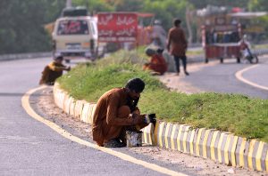 Labourers painting roadblocks near Head Muhammad Wala Road as part of ongoing measures to regulate traffic and prevent accidents.
