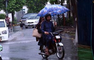 A motorcyclist balances his ride with an umbrella in hand to shield himself from heavy rainfall while passing through the city.