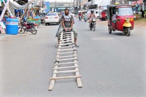 A worker balances a long wooden ladder on a motorcycle along Hazoori Bagh Road in Multan.