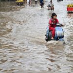 Vehicles pass through accumulated rainwater on a road during rainfall in the provincial capital