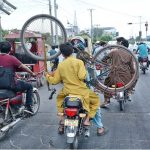 A youngster transports a bicycle by holding it while riding on the back of a motorcycle
