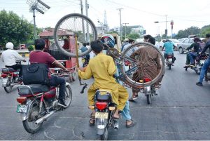 A youngster transports a bicycle by holding it while riding on the back of a motorcycle