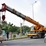 Labourers sitting in the pocket of a loader crane while heading to a worksite on Walton Road