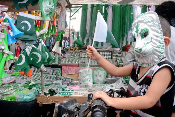 A child wearing a mask purchasing Independence Day celebration items in the Saddar area