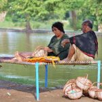 A woman engaged in preparing handmade baskets while sitting on a traditional charpai along the canal bank to earn livelihood.