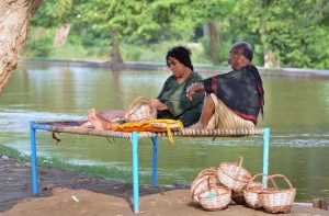 A woman engaged in preparing handmade baskets while sitting on a traditional charpai along the canal bank to earn livelihood.
