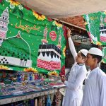 Youngsters displaying flags and badges at a roadside stall in connection with Rabi-ul-Awal celebrations.