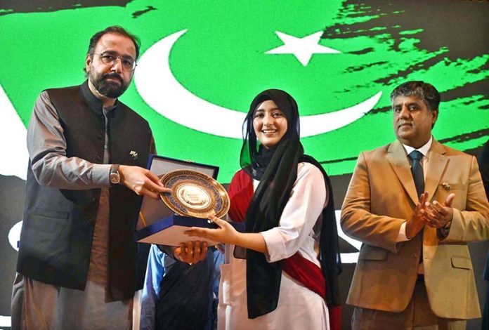 Federal Minister for Overseas Pakistanis and Human Resource Development, Chaudhry Salik Hussain, awarding a shield to young female achiever during the Marka-e-Haq and 78th Independence Day celebrations organized by the Workers Welfare Fund at the National Library Auditorium