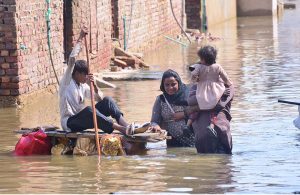 Rain-affected residents of Fatima Jinnah Colony use a makeshift boat made of wood and air-filled bags to pass through flooded streets after torrential rain in the city last night.