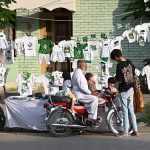 A motorcyclist along with his children buying festive items, including a national flag and outfits printed in national colours, from a roadside stall in connection with Independence Day celebrations