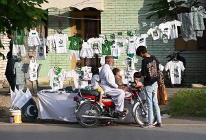 A motorcyclist along with his children buying festive items, including a national flag and outfits printed in national colours, from a roadside stall in connection with Independence Day celebrations