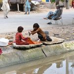 Girls wash clothes while sitting along the canal bank