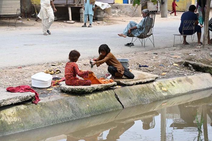 Girls wash clothes while sitting along the canal bank