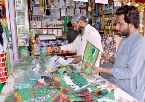 A man buys a religious flag from a shopkeeper ahead of 12 Rabi-ul-Awwal celebrations at Railway Station Road in Quetta.