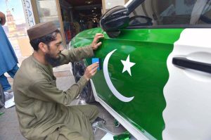 A man carefully pasting a national flag sticker on a vehicle as part of preparations for Independence Day celebrations at FC Chowk.