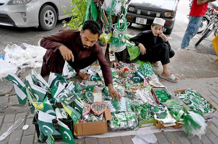 A street vendor arranges festive items to attract patriotic passers-by ahead of Independence Day celebrations at a roadside stall in the federal capital