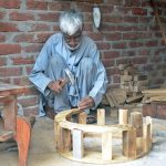 An elderly worker busy making wooden table at his workplace in the furniture market.