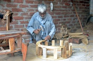 An elderly worker busy making wooden table at his workplace in the furniture market.