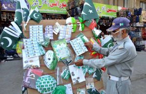 A traffic police officer browsing national flag badges at a festive items stall to purchase for Independence Day celebrations on Jinnah Road.