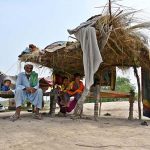Flood-affected residents of Mehbob Kalhoro village in the Kachha area of the Indus River sit in makeshift huts along the Larkana-Khairpur road after the district administration issued a flood warning