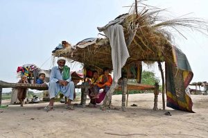 Flood-affected residents of Mehbob Kalhoro village in the Kachha area of the Indus River sit in makeshift huts along the Larkana-Khairpur road after the district administration issued a flood warning