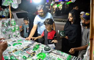 A family selecting to purchase national flag and festive items from a vendor’s stall in connection with the 78th Independence Day Marka-e-Haq celebrations.