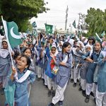 Students hoist the national flag during the TMC Korangi rally passing through Korangi area in connection with the Marka Haq celebration