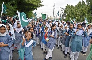 Students hoist the national flag during the TMC Korangi rally passing through Korangi area in connection with the Marka Haq celebration