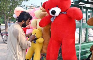 A vendor decorates and displays children’s soft toys to attract customers at his roadside setup