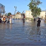 People wade through a road inundated by floodwaters on Shafi Da Bhatta, Bhagowal Road in southern Sialkot