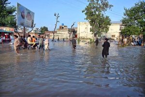 People wade through a road inundated by floodwaters on Shafi Da Bhatta, Bhagowal Road in southern Sialkot