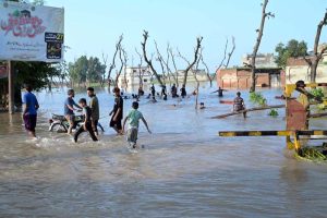 People wade through a road inundated by floodwaters on Shafi Da Bhatta, Bhagowal Road in southern Sialkot