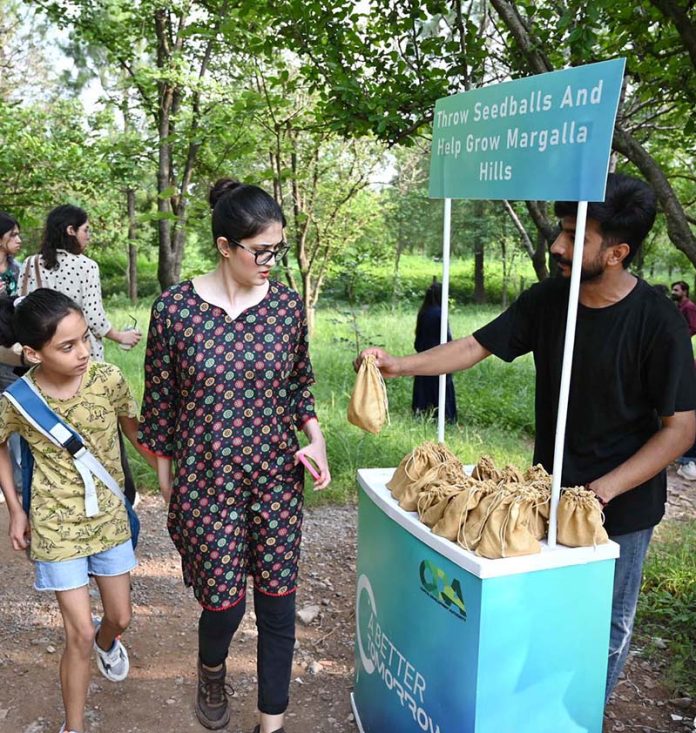 A volunteer distributes seed balls to visitors during the 'Seed Ball Distribution Campaign' organized by Pakistan Tobacco Company (PTC) in collaboration with the Capital Development Authority (CDA) at Trail 5 entrance, encouraging efforts to green the Margalla Hills
