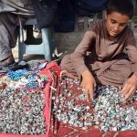 A young gemstone vendor displays rings to attract passersby at his roadside stall in Chaman Phatak, Quetta