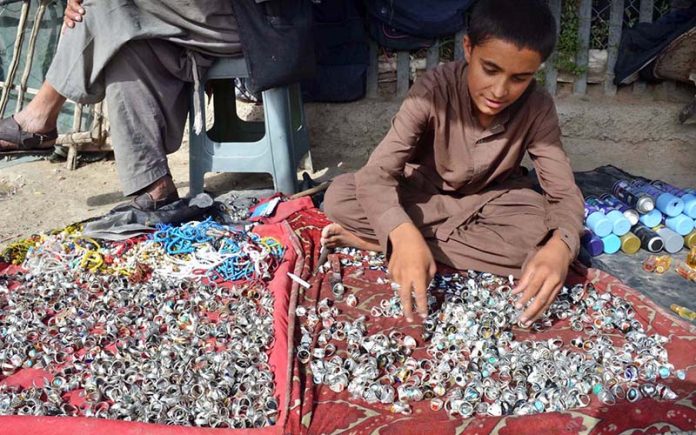 A young gemstone vendor displays rings to attract passersby at his roadside stall in Chaman Phatak, Quetta