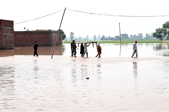 Residents carrying local bed (Charpai) passing through floodwaters to safe place in the Mandi Faizabad District Nankana