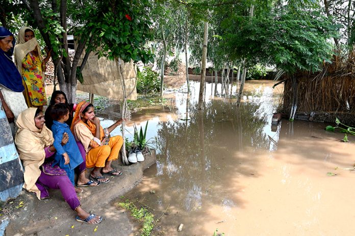 A family sitting outside their house submerged in flood water at Mandi Faizabad district Nankana