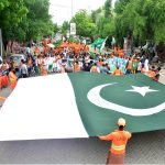 Workers of Sindh Solid Waste Management Board holding rally with displaying huge national flag during the 78th Independence Day and Maarka-E-Haq celebrations at Radio Pakistan Road