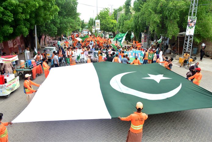 Workers of Sindh Solid Waste Management Board holding rally with displaying huge national flag during the 78th Independence Day and Maarka-E-Haq celebrations at Radio Pakistan Road