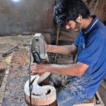 A carpenter is busy carving designs on a wooden piece at his workplace in Dhoke Kala Khan.