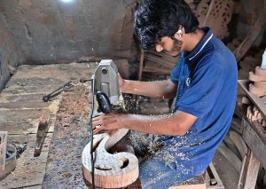 A carpenter is busy carving designs on a wooden piece at his workplace in Dhoke Kala Khan.