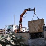 Workers using a crane to lift and install heavy concrete blocks for roadside construction at 10th Avenue Flyover in the Federal Capital