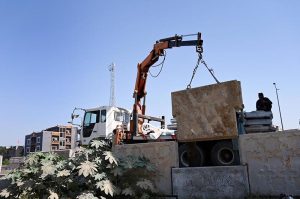 Workers using a crane to lift and install heavy concrete blocks for roadside construction at 10th Avenue Flyover in the Federal Capital