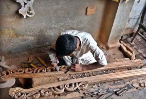 A carpenter is busy carving designs on a wooden piece at his workplace in Dhoke Kala Khan.