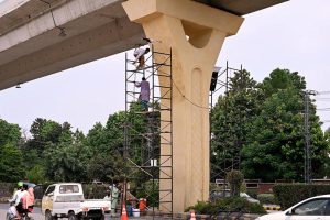 A worker busy painting the underside of a flyover while standing in a crane-mounted basket as part of ongoing maintenance work at Peshawar mor interchange in the Federal Capital.