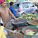 A vendor busy in roasting corn cobs to attract customers at his roadside setup in Federal Capital