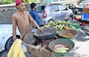 A vendor busy in roasting corn cobs to attract customers at his roadside setup in Federal Capital