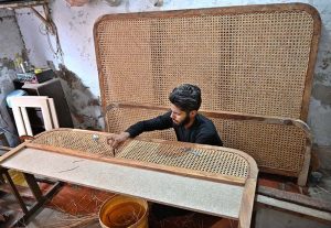 A carpenter is busy carving designs on a wooden piece at his workplace in Dhoke Kala Khan.