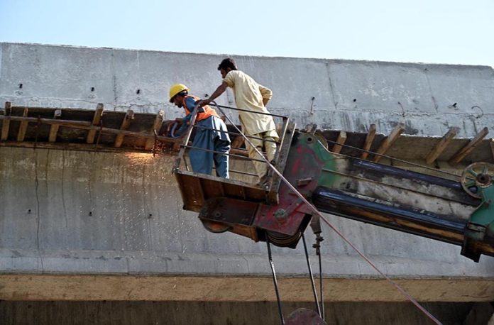 Workers busy welding during the construction work of 10th Avenue Flyover with the help of a crane in the Federal Capital