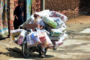 A view of daily toil as an elderly motorcyclist balances a stack of chips and snake packets on his motorcycle during a delivery in Latifabad